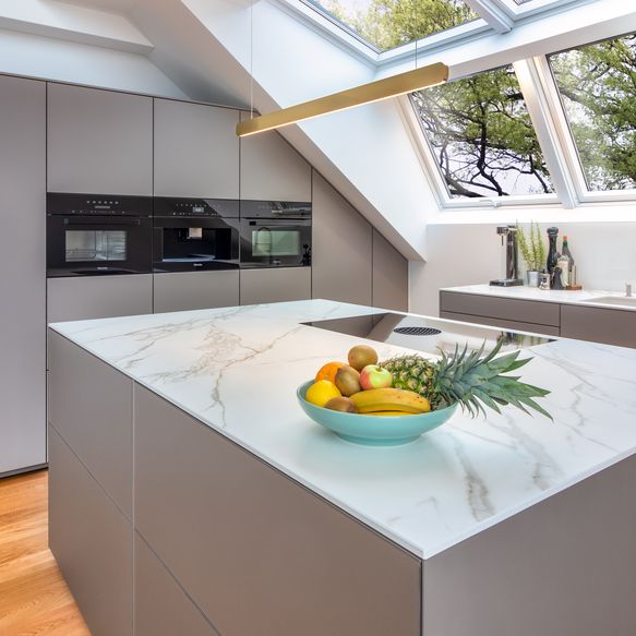 Graue Küche und weiß-marmorierte Arbeitsplatte, einzeilig mit Insel und Schrankwand unter Dachschräge