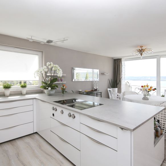 Weiße, offene Küche im U-Form mit hellgrauer Arbeitsplatte und filigranen Griffen