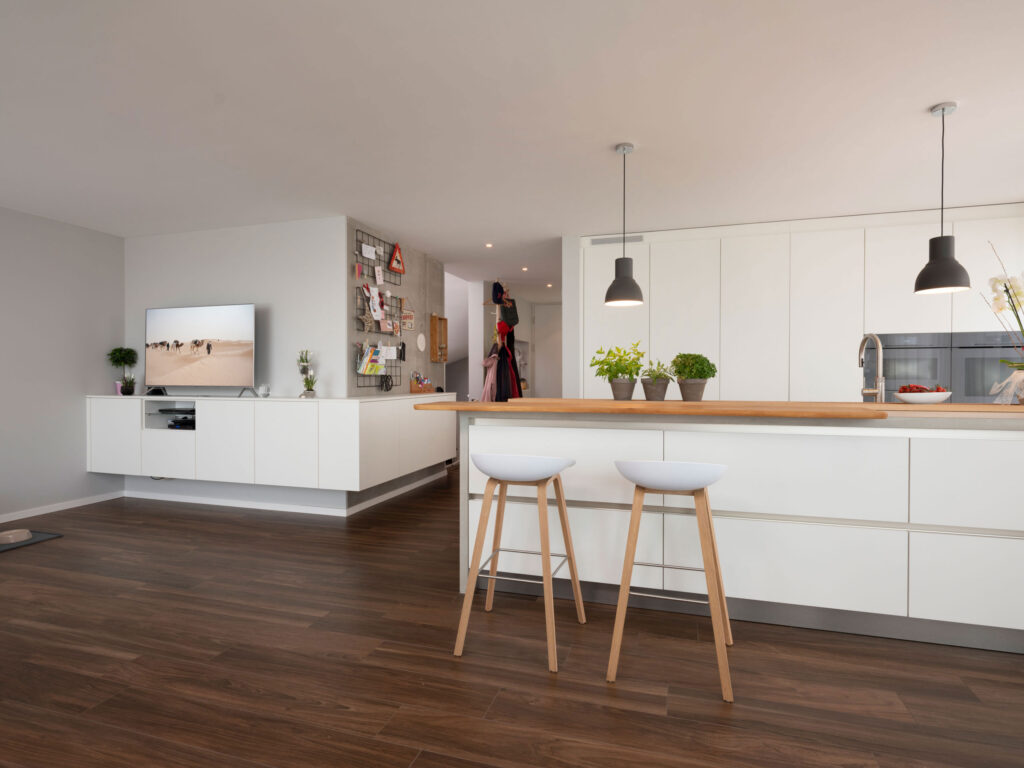 Weiße Wohnküche mit Hochschrankwand, langer Insel und TV-Schrank mit Ablagefläche