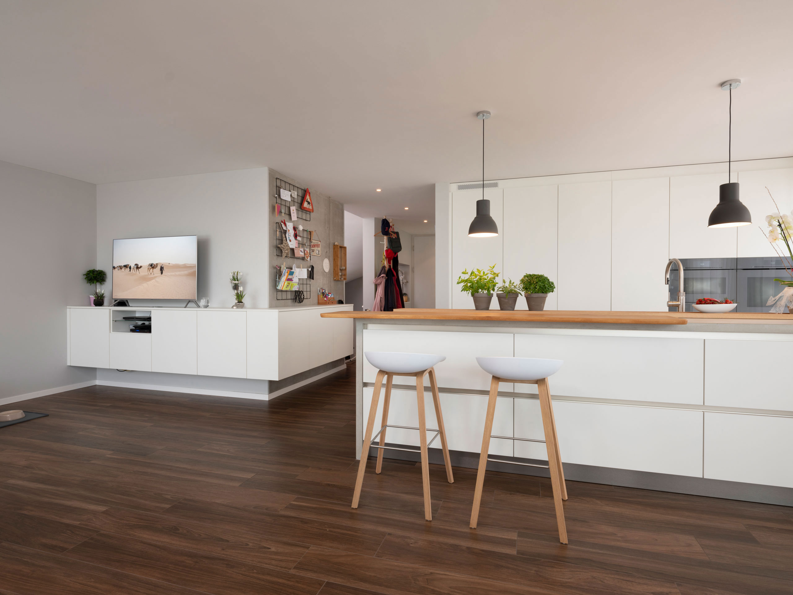 Weiße Wohnküche mit Hochschrankwand, langer Insel und TV-Schrank mit Ablagefläche