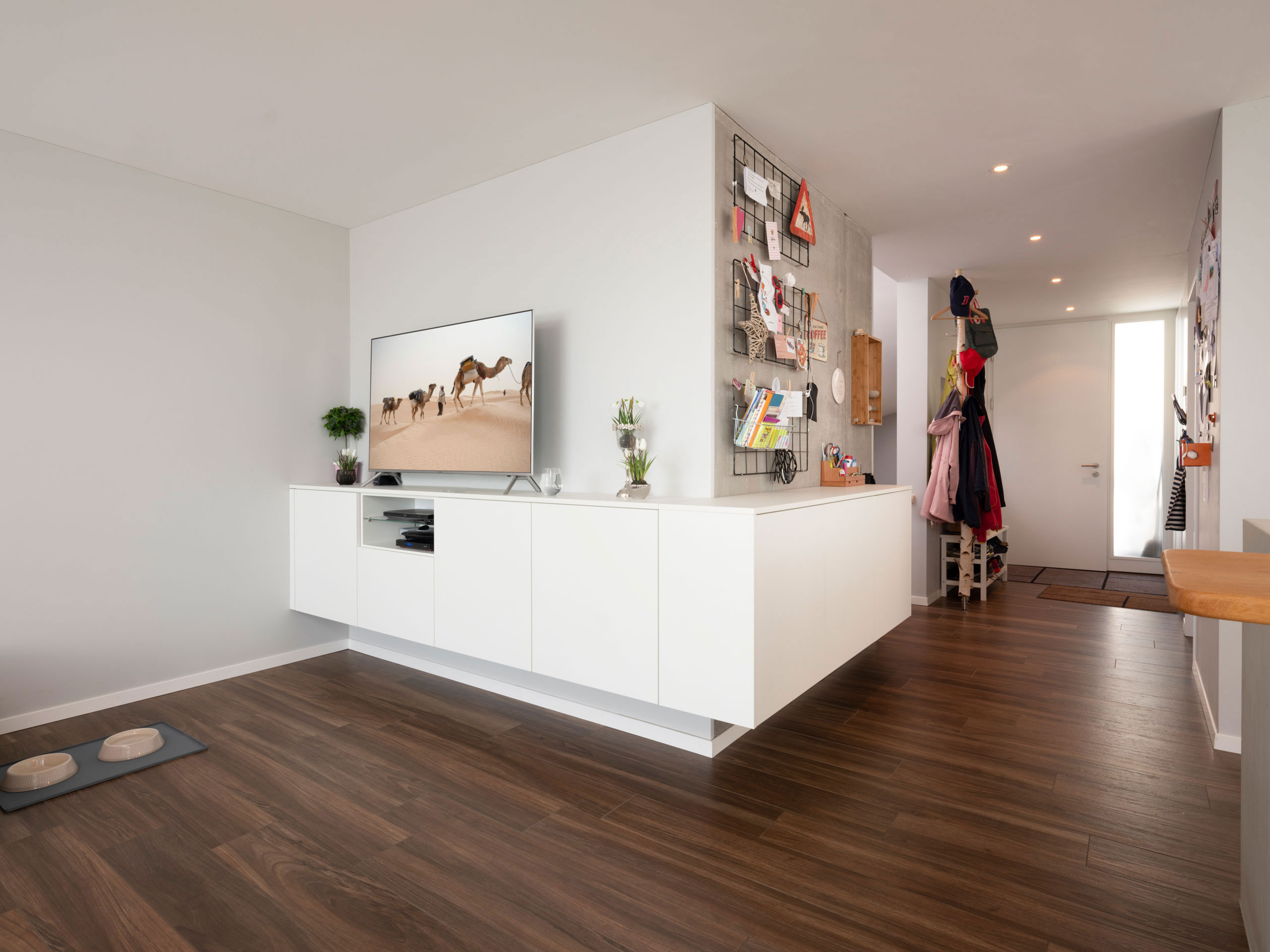 Weiße Wohnküche mit Hochschrankwand, langer Insel und TV-Schrank mit Ablagefläche