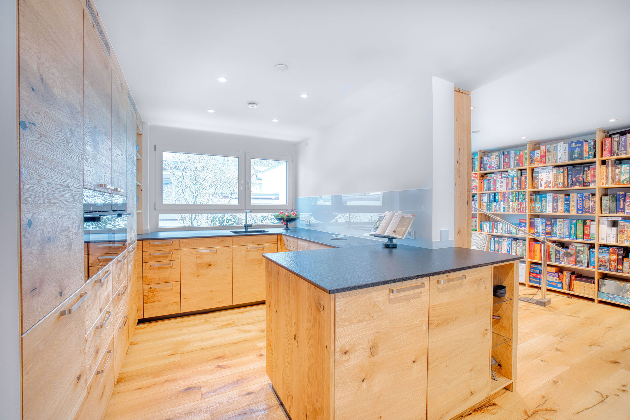 Helle Massivholzküche mit dunkler Arbeitsplatte aus Naturstein mit passendem Bücherregal