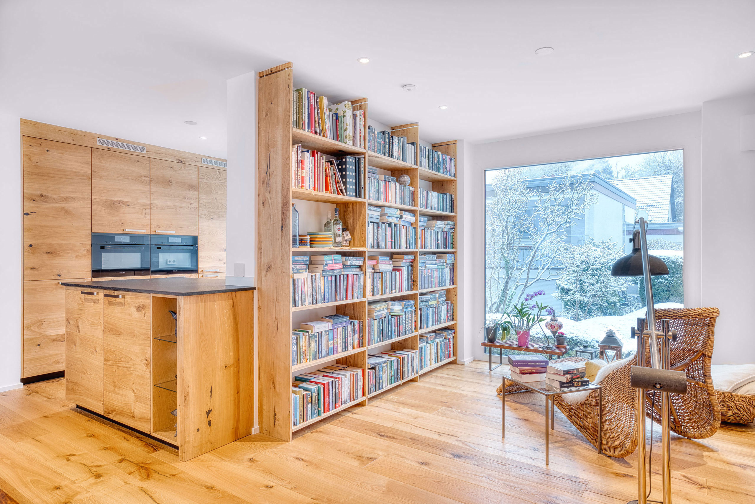 Helle Massivholzküche mit dunkler Arbeitsplatte aus Naturstein mit passendem Bücherregal