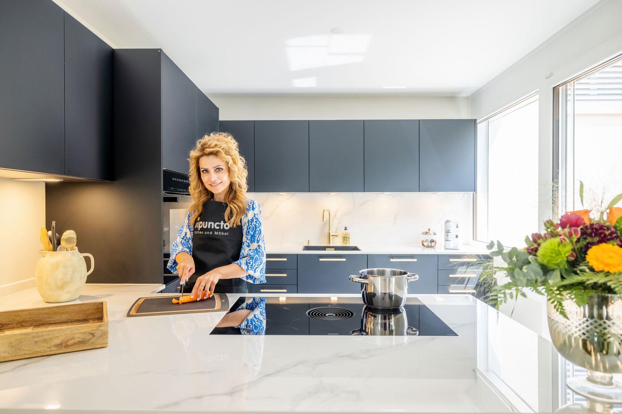 Edle Küche in U-Form in schwarz-weiß und goldenen Details und kochende Frau