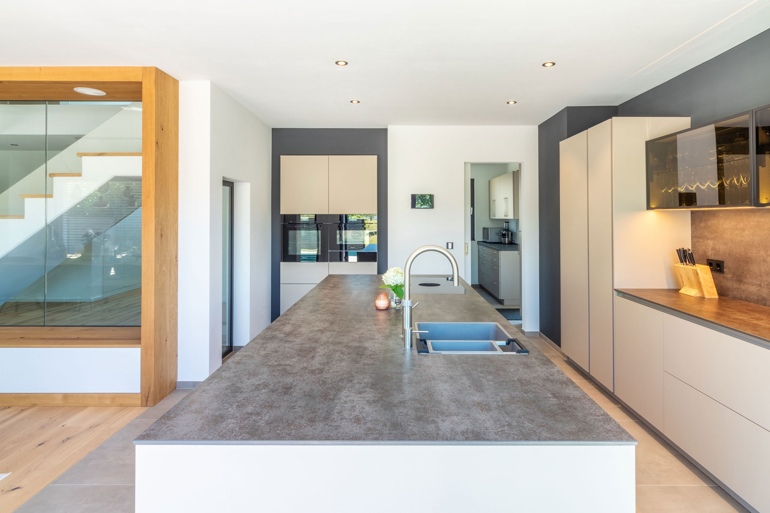 Küche in beige mit Kochinsel und langer Zeile mit Glas-Elementen