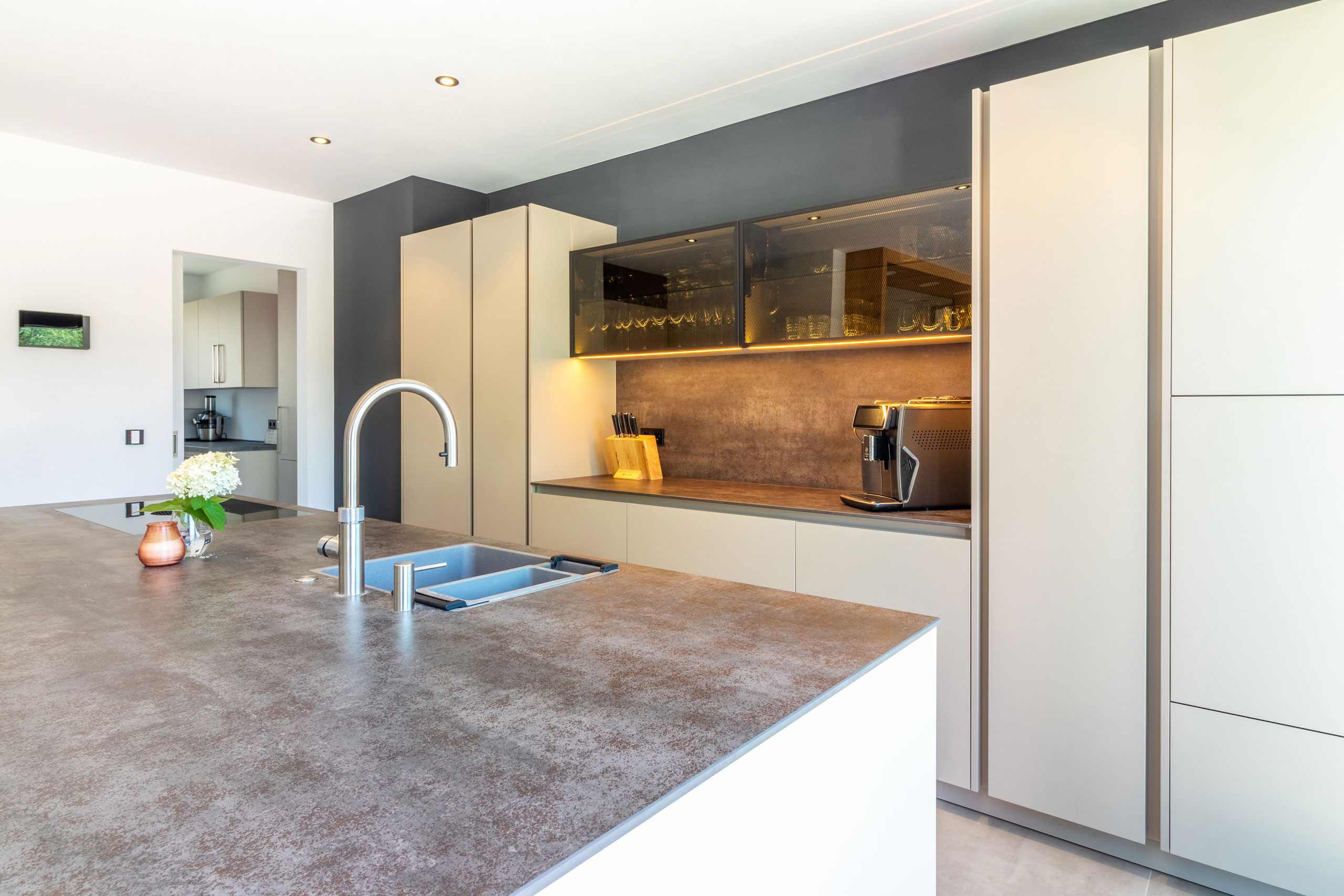 Küche in beige mit Kochinsel und langer Zeile mit Glas-Elementen