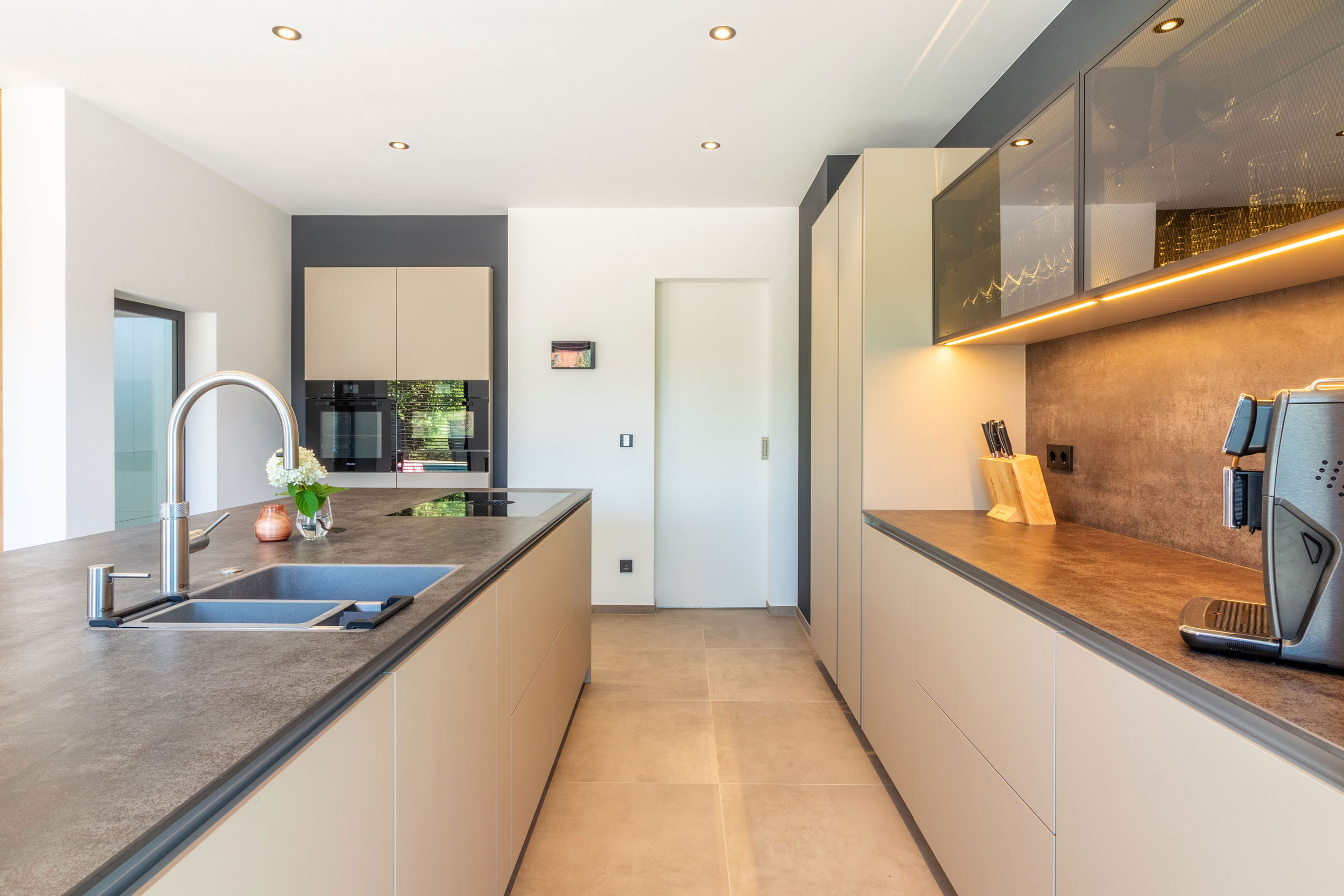 Küche in beige mit Kochinsel und langer Zeile mit Glas-Elementen
