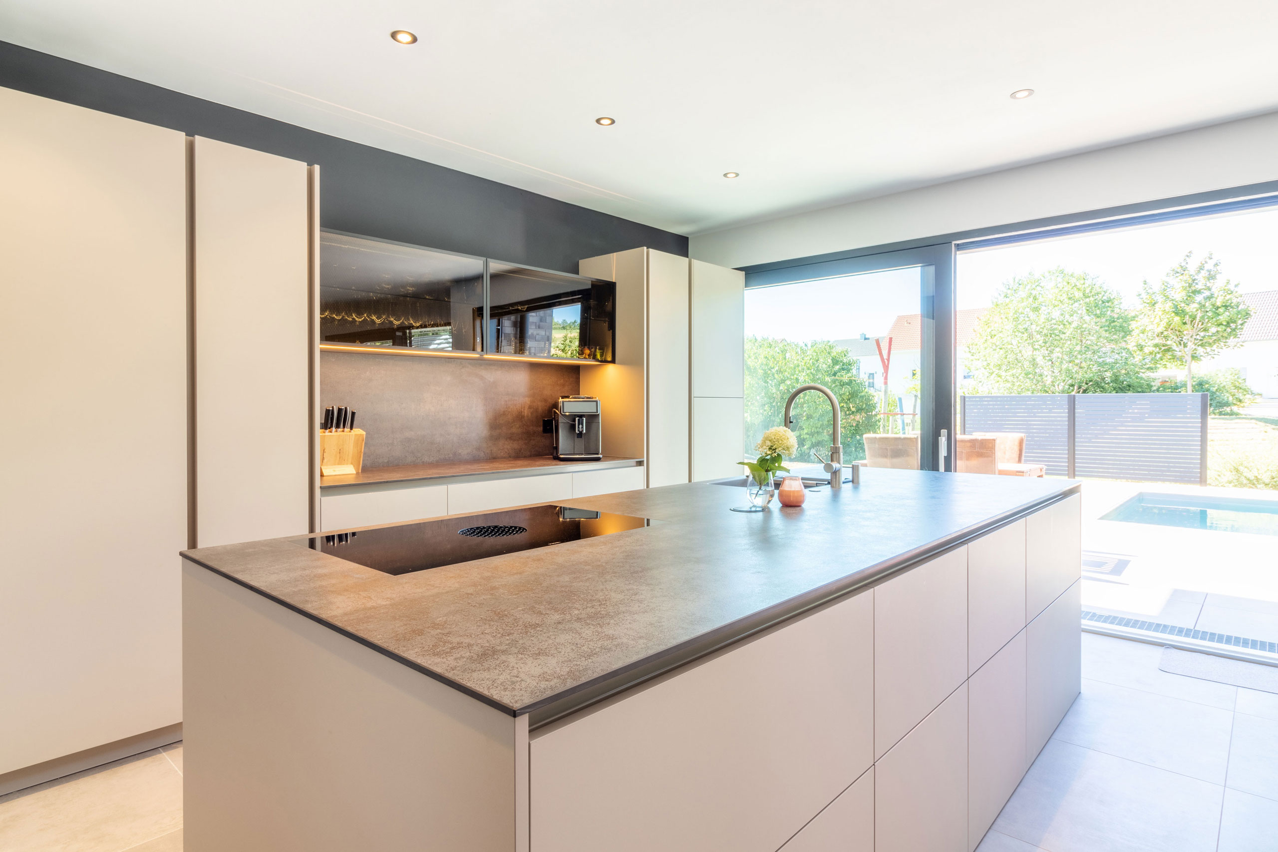 Küche in beige mit Kochinsel und langer Zeile mit Glas-Elementen