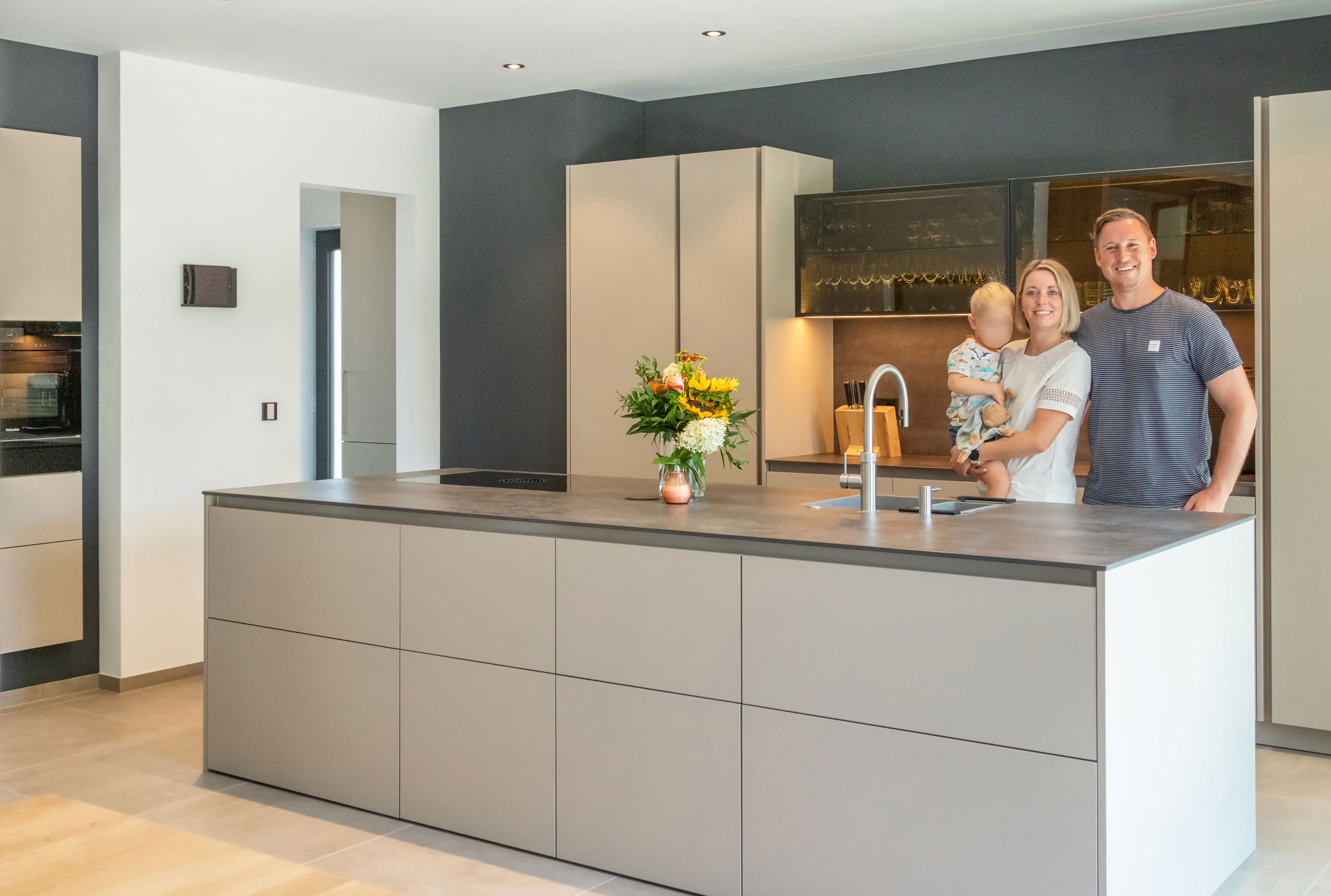 Küche in beige mit Kochinsel und langer Zeile mit Glas-Elementen und Familie