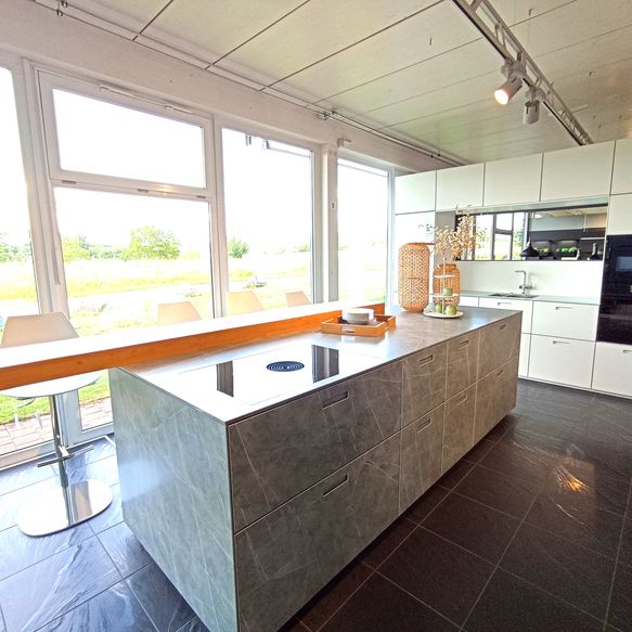 Weiße Küchenzeile mit vielen Schränken und großer Insel mit Bartop und großes Holzregal