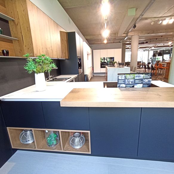 Ausstellungsküche mit dunklen Fronten und Holzoptik in T-Form mit egalen