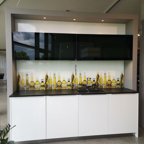 Ausstellungsküche mit Küchenzeile bestehend aus weißen hochglanz Unterschränken, Oliven-Glas-Rückwand und schwarzen Glas-Oberschränken