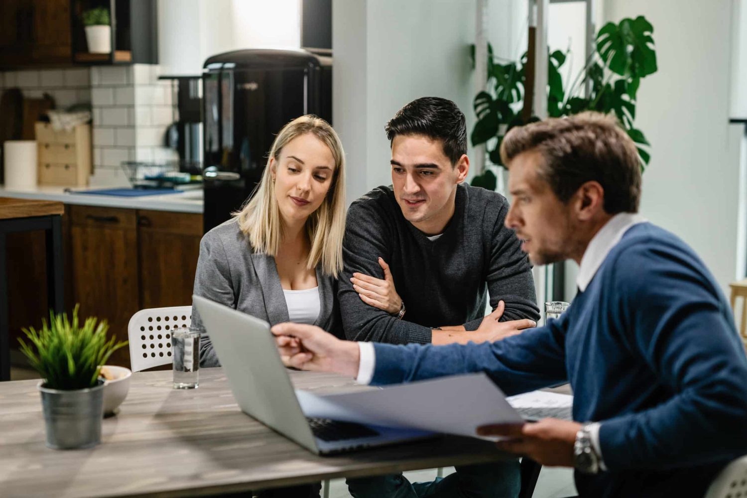 Young couple and real estate agent using laptop while going through housing plan on a meeting.