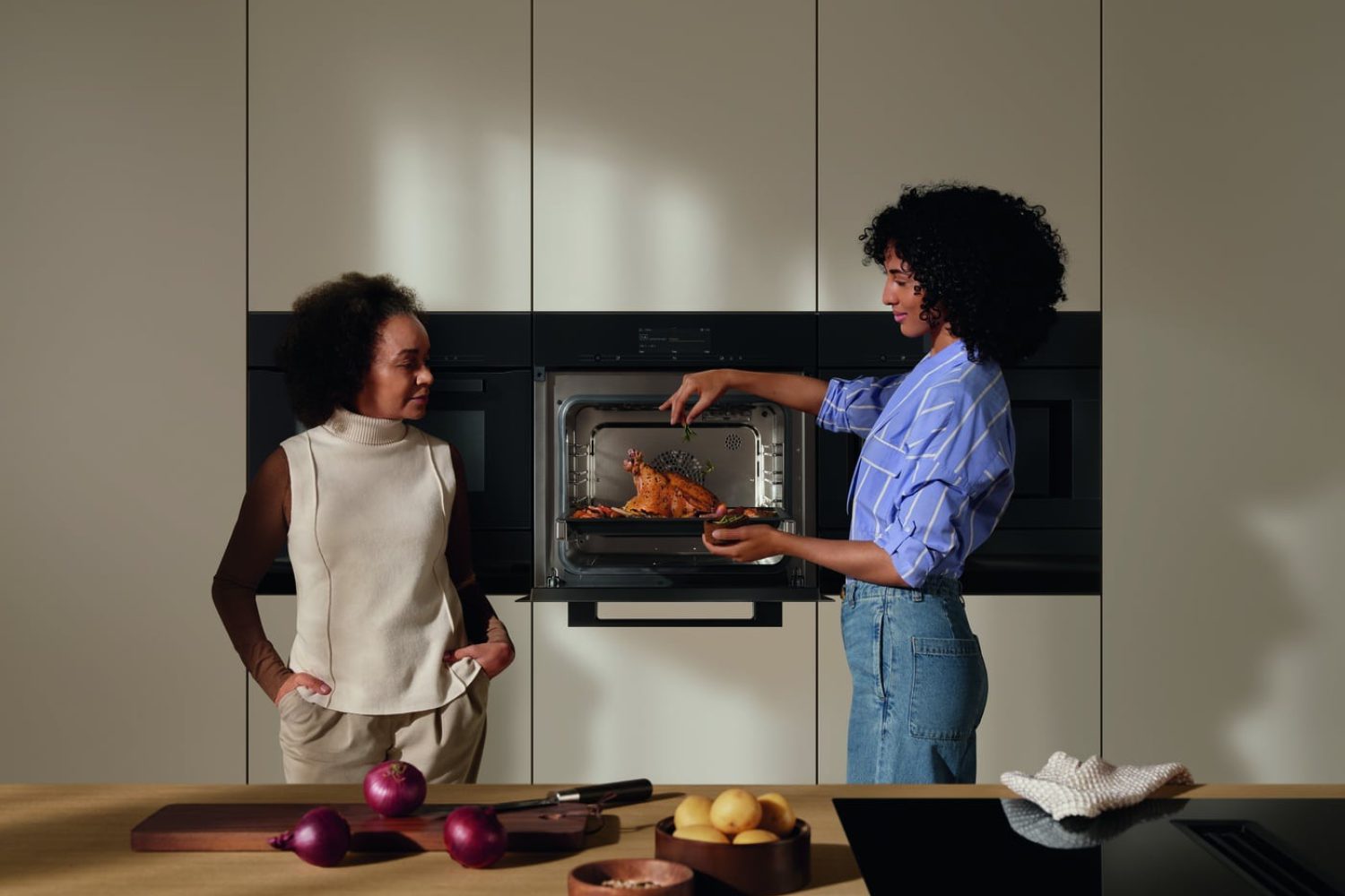Dampfbacköfen von Miele in brauner Küche und zwei Damen die kochen