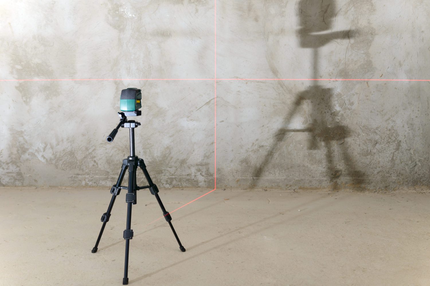 The laser level projects red lines onto the wall with a rough finish
