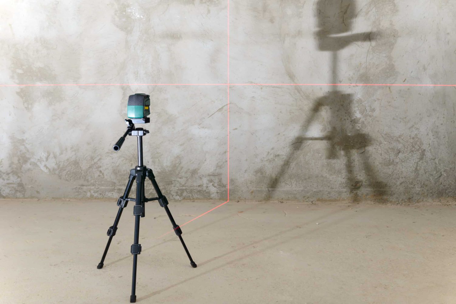 The laser level projects red lines onto the wall with a rough finish